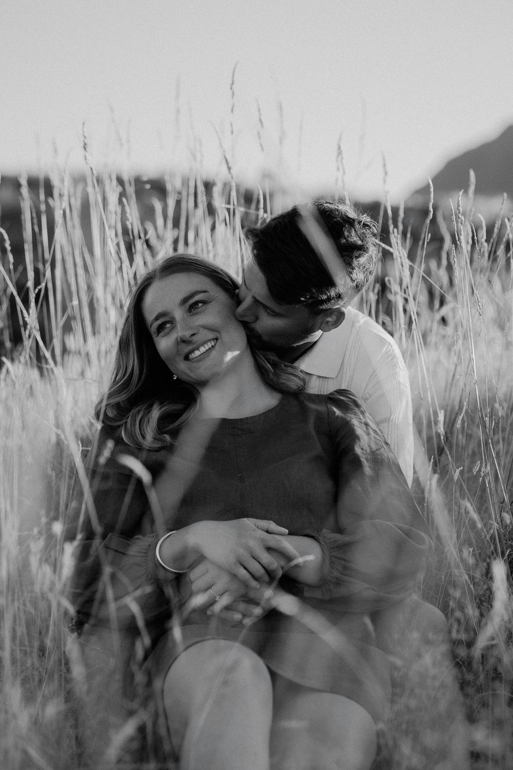 Romantic black and white photo series of a couple laughing together in tall grass at sunset.