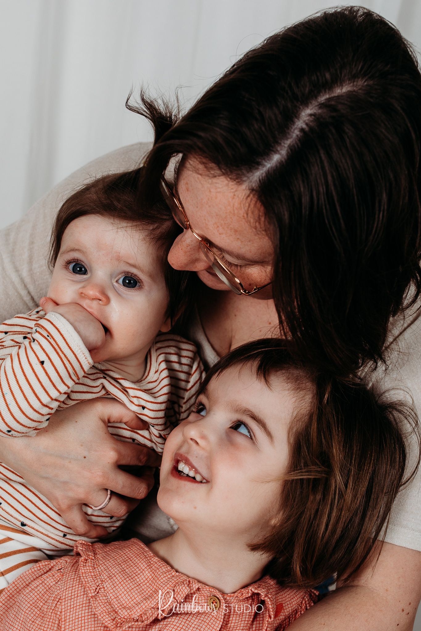 Mama met haar 2 dochters. Een mooie familie. Mama en de oudste dochter kijken naar de jongste terwijl zij de camera inkijkt.