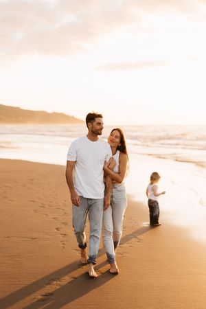Family strolling on sandy beach during golden hour as waves roll in.