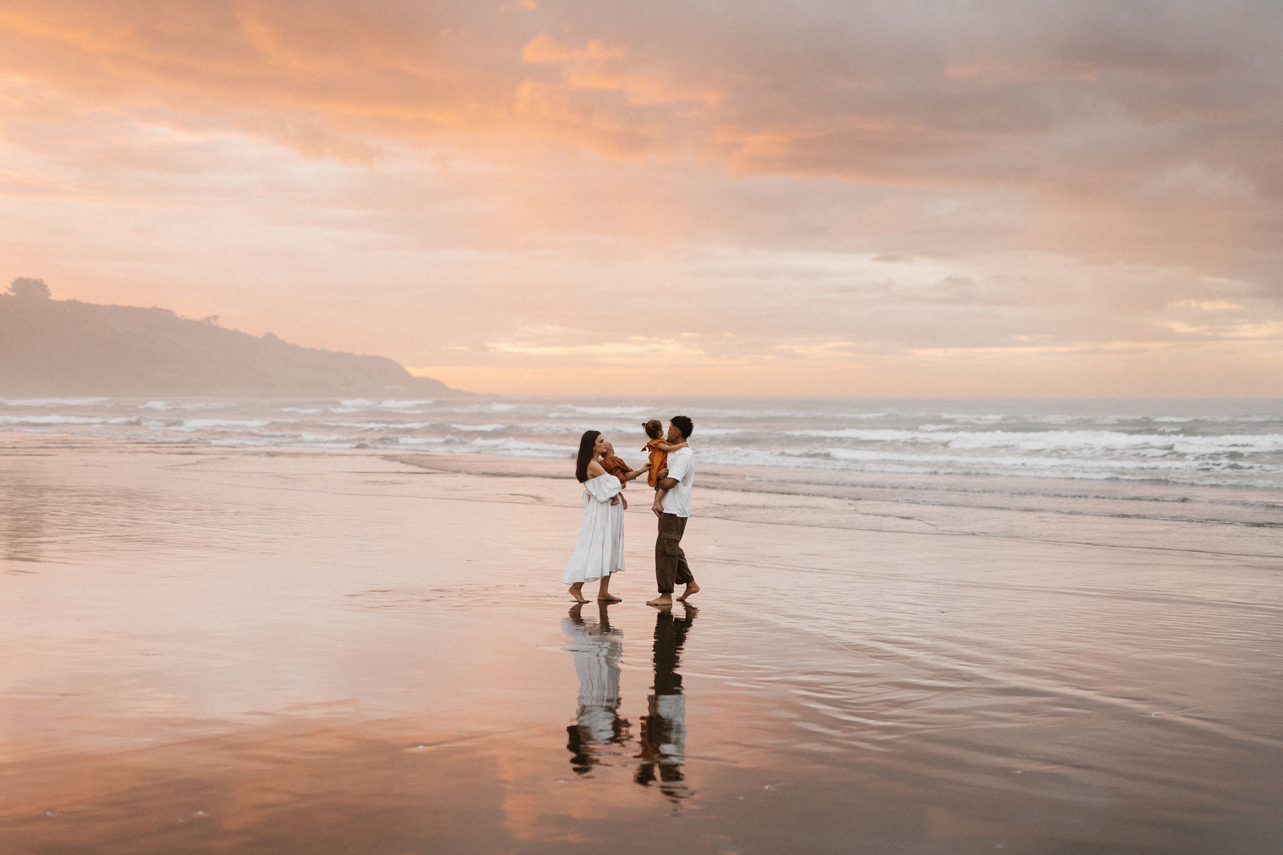 Family interacting on reflective beach during vibrant orange sunset.