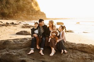 Family sitting together on coastal rocks during sunset by the ocean.
