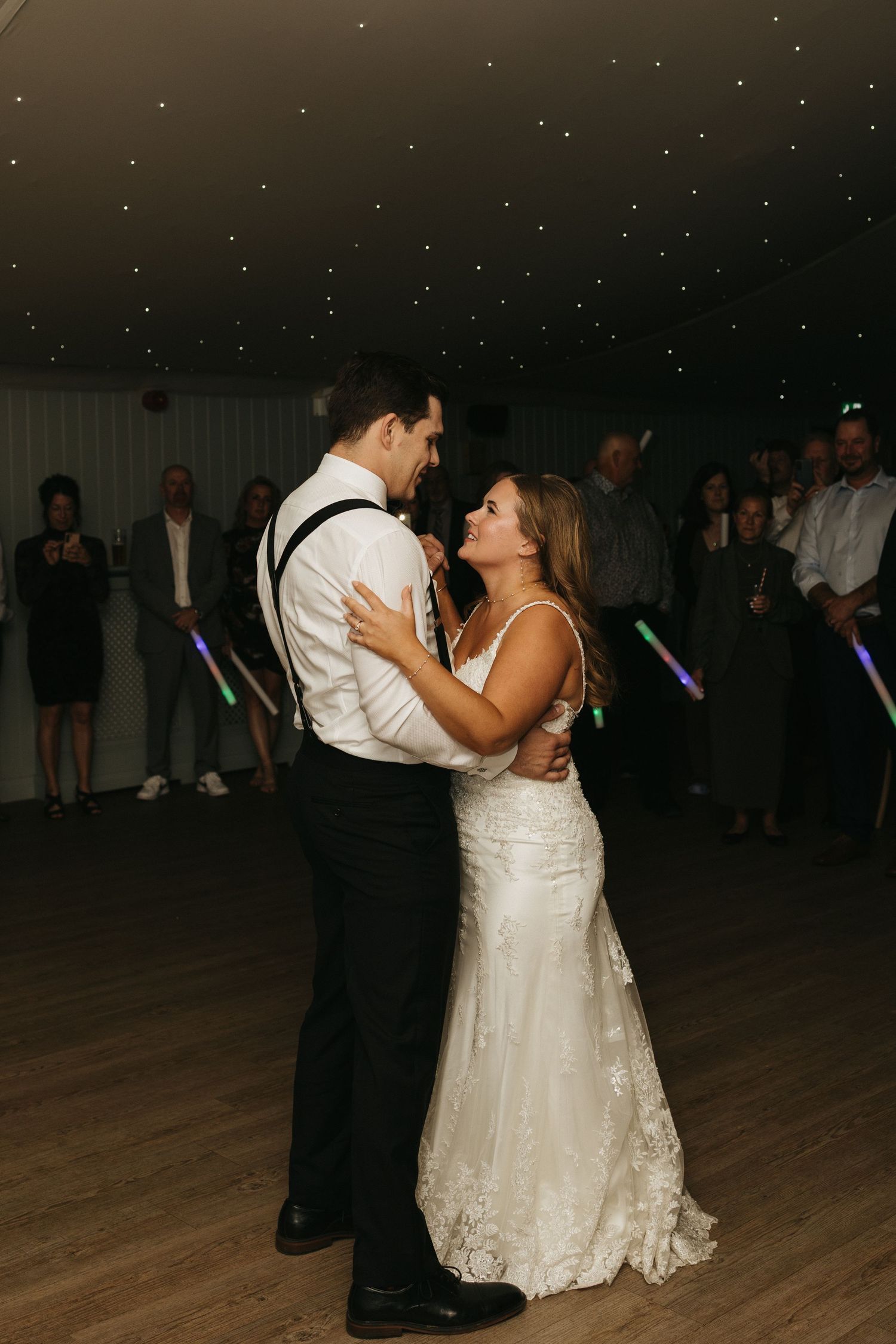 Newlywed couple shares a romantic dance together during their wedding reception on a wooden dance floor.