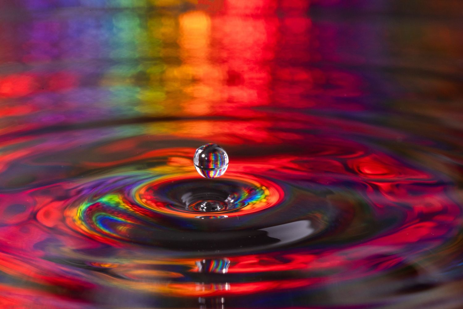 A sequence of colorful water drops creating ripple effects with red and purple lighting in macro photography.