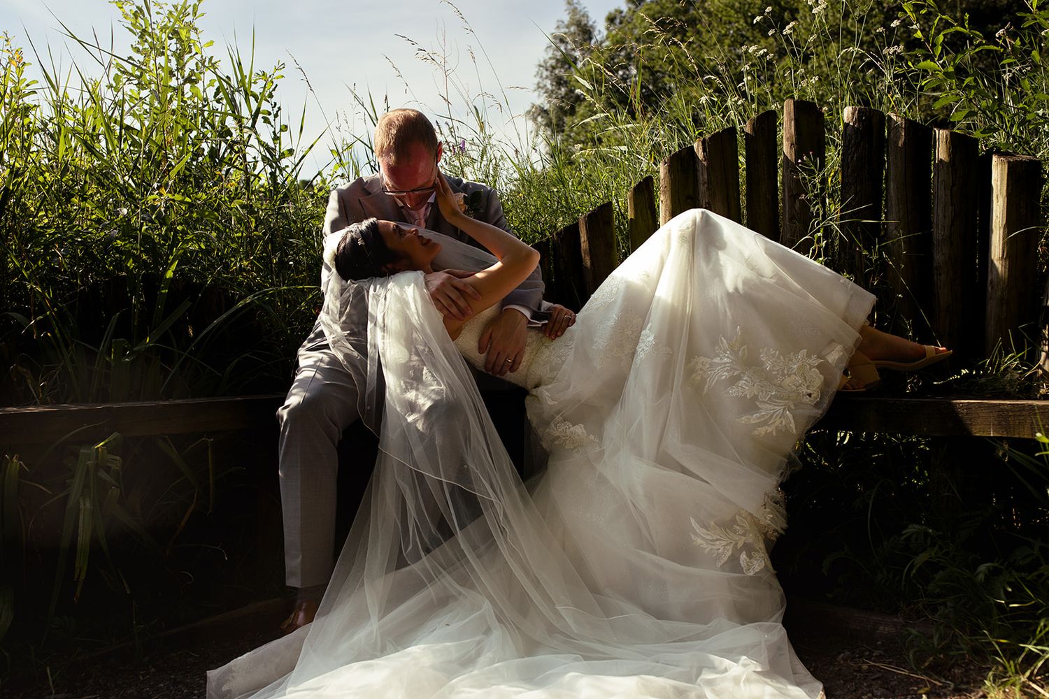 Bride and groom share a romantic moment on a wooden seat surrounded by lush greenery at Brockholes Nature Reserve, Preston. Jane Ball Photog