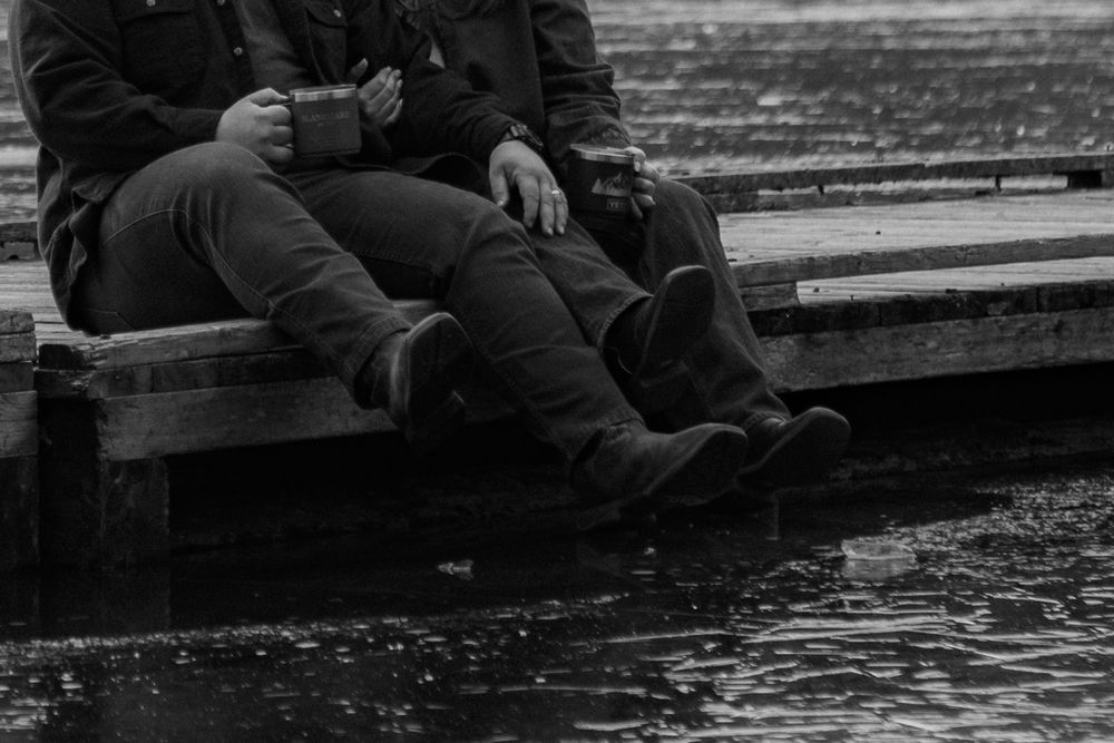 A black and white image shows a person sitting alone on a bench, with their head down and their hands folded in their lap.