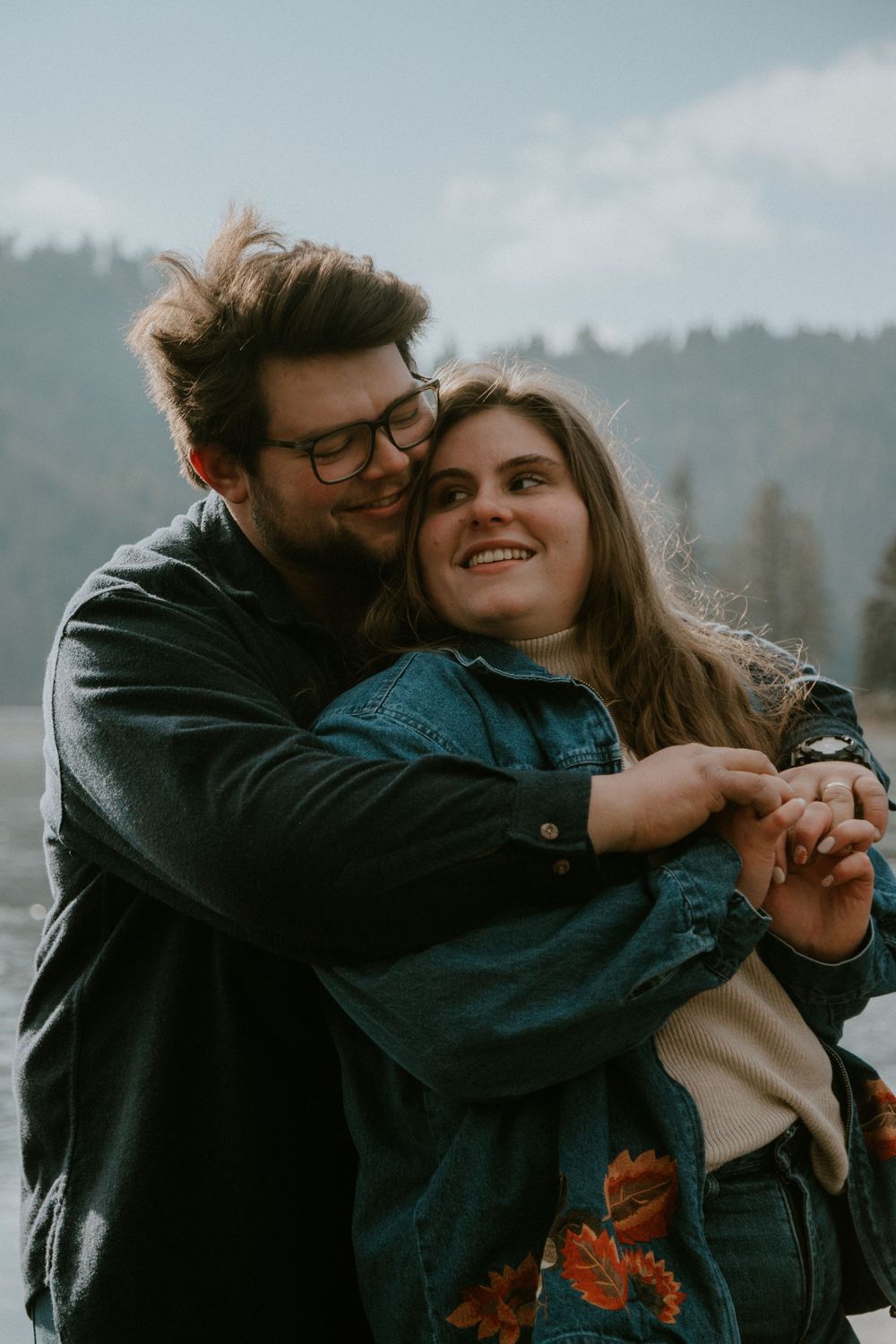 A happy couple embracing outdoors with a scenic mountain landscape in the background.