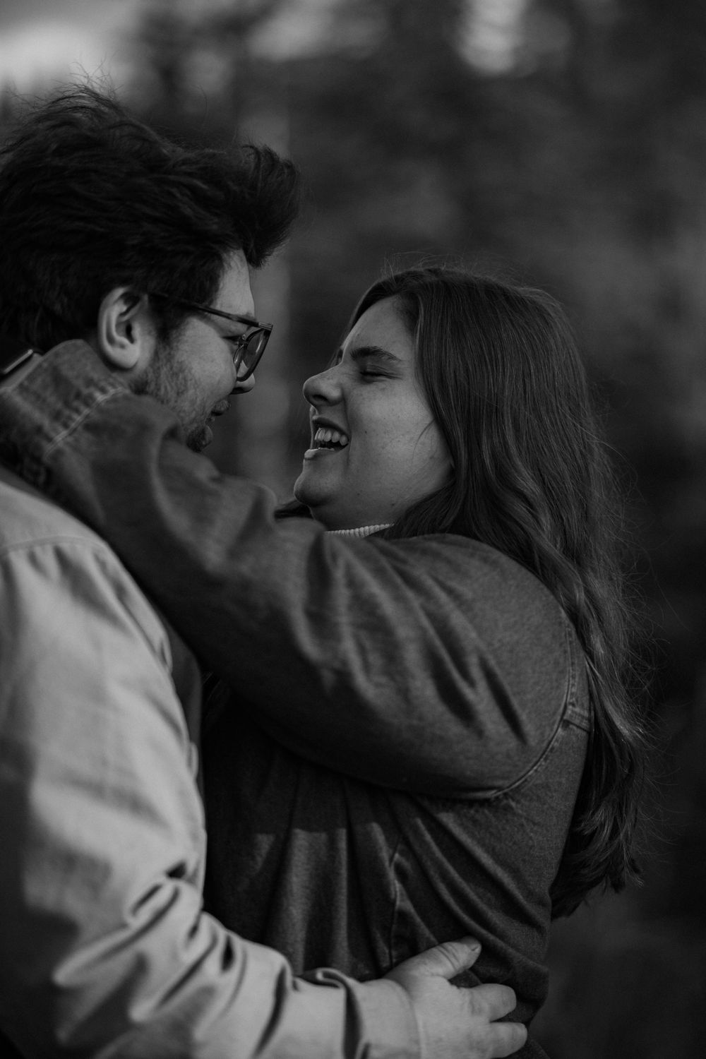 A black and white image showing a loving couple embracing and gazing into each other's eyes in a natural outdoor setting.
