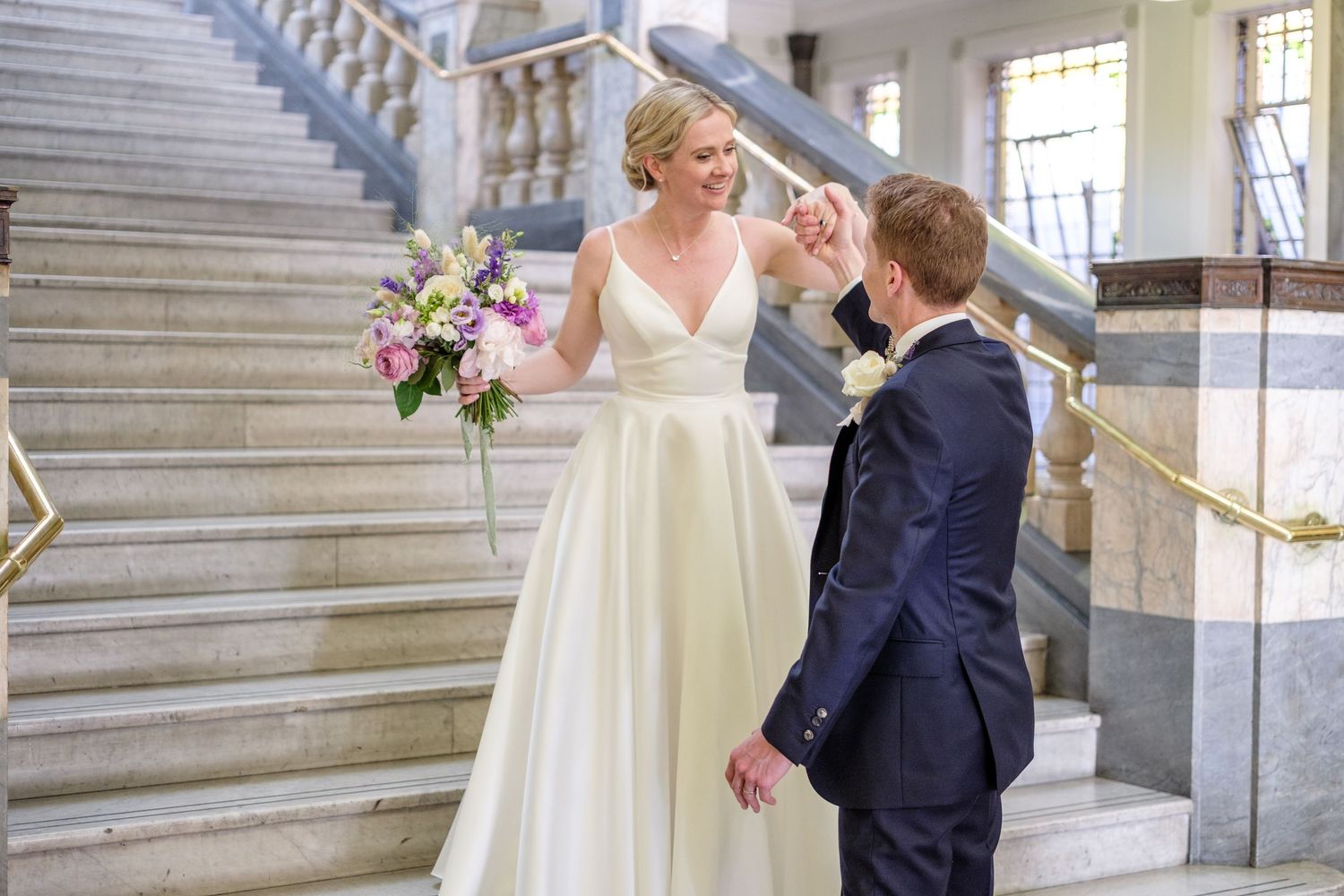 A bride in a white wedding gown and a groom in a dark suit embrace on a grand staircase.