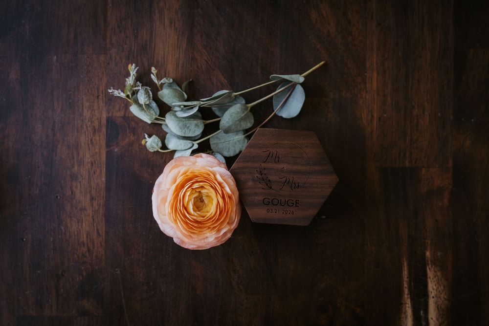 Peach ranunculus flower and eucalyptus sprig in a hexagonal wooden vase on a dark wood surface.