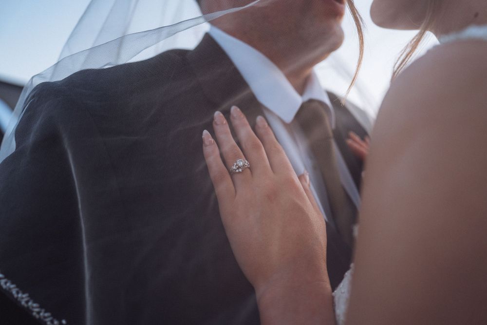 Close-up of bride's hand with stunning diamond engagement ring resting on groom's dark suit jacket.