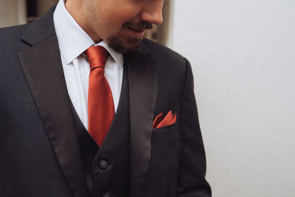 Man in black tuxedo with red tie and matching pocket square, elegant formal attire for wedding or event.