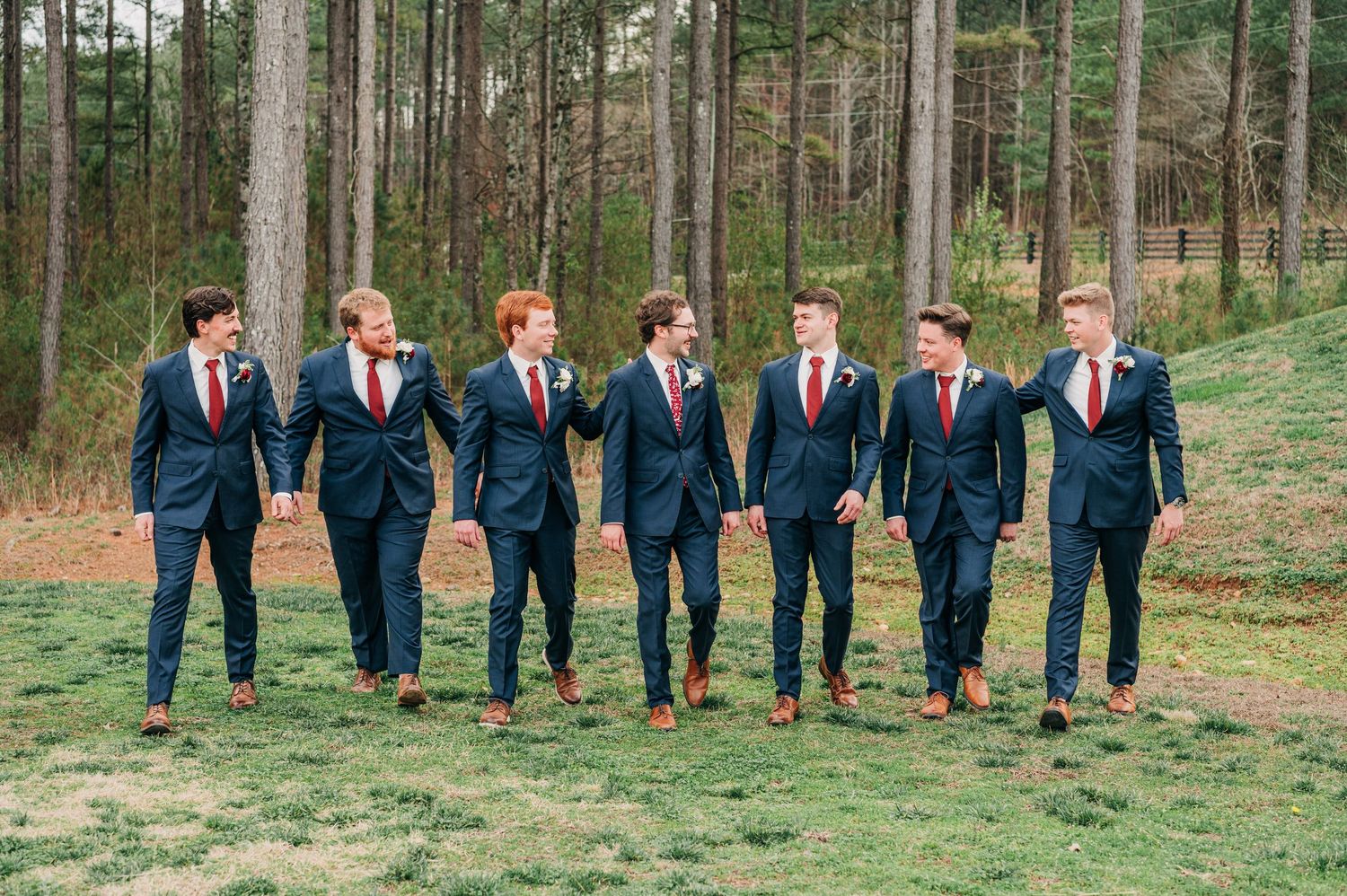 Wedding party in navy suits walking together through a scenic wooded forest setting.