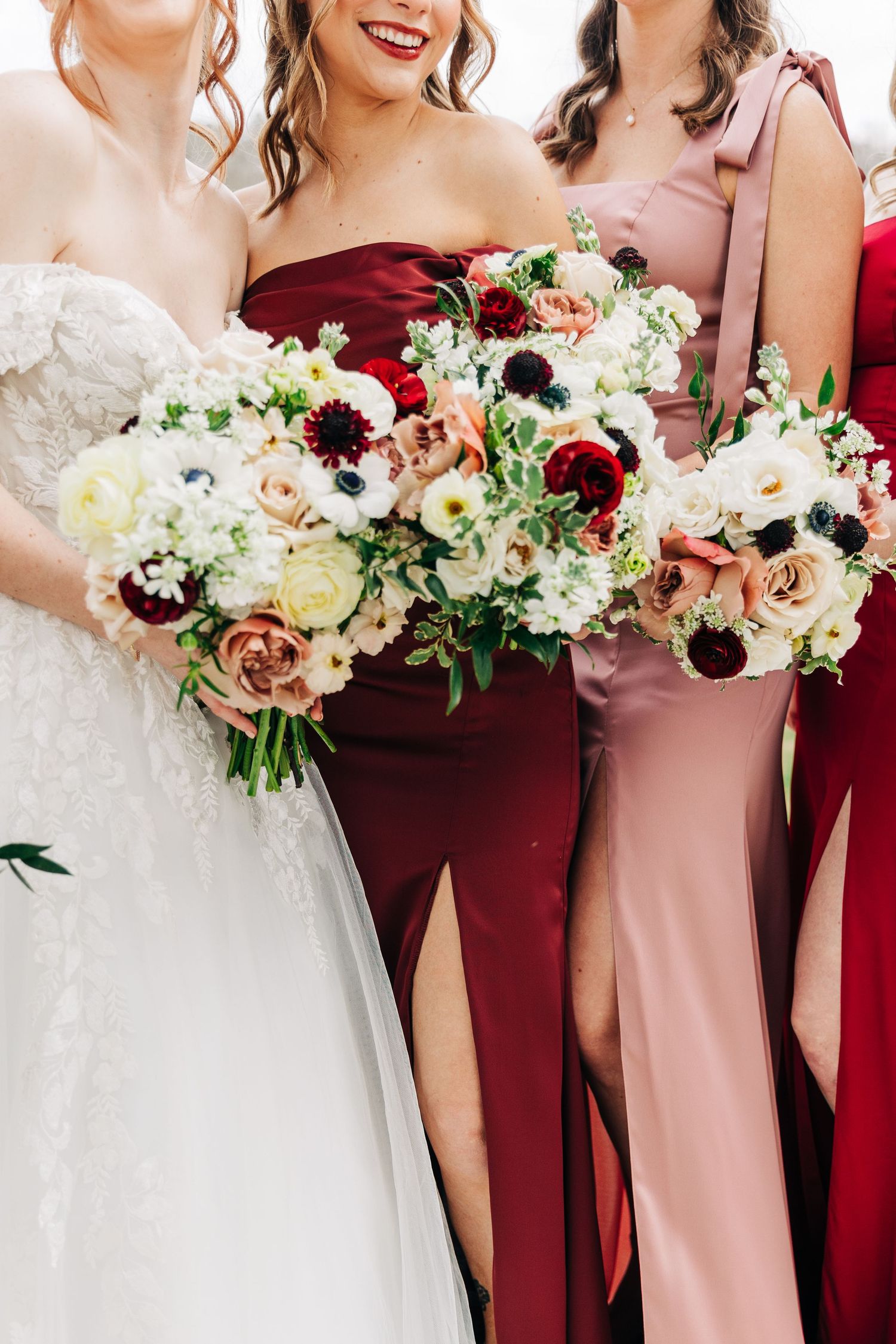Elegant wedding party lineup showcasing burgundy and blush pink bridesmaid dresses with white floral bouquets.