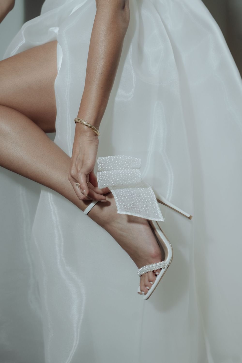 Bride fastening pearl-embellished white stiletto heels against flowing white wedding gown.