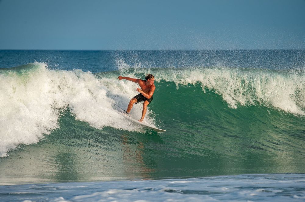 A surfer rides a turquoise wave while performing a dynamic cutback maneuver against white ocean spray.