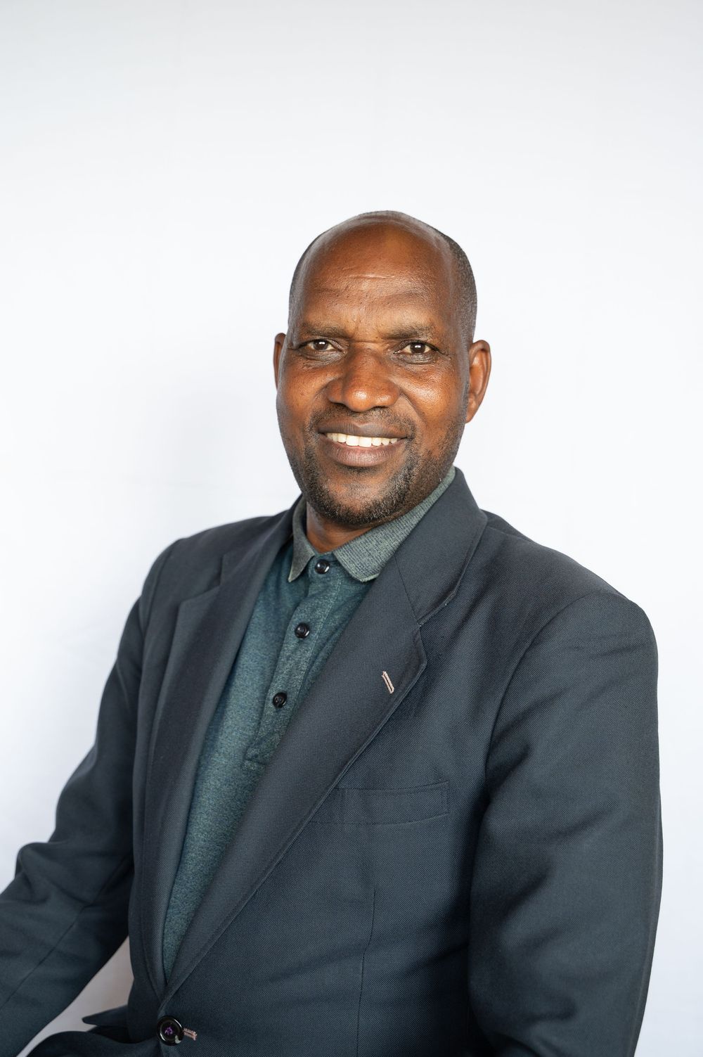 Professional headshot of a person in a dark blazer and green polo shirt smiling against a white backdrop.