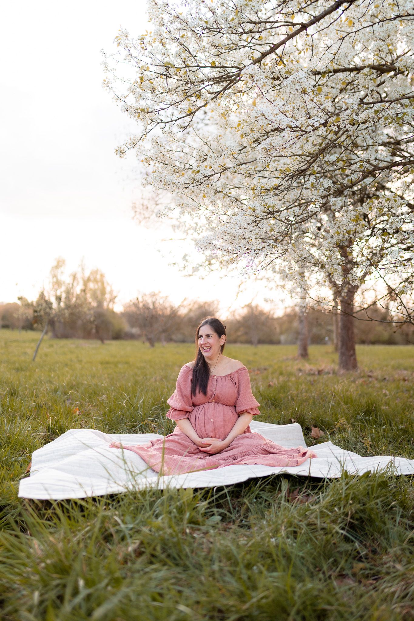 Future maman souriante assise dans l’herbe sous un arbre en fleurs au printemps