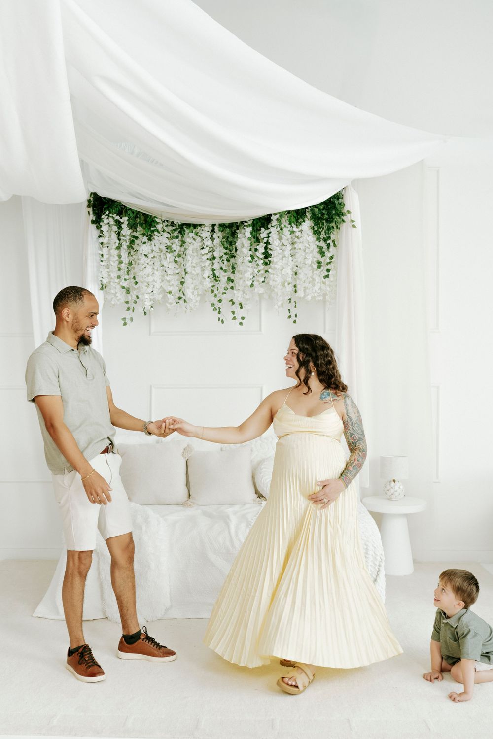 A family plays together in a bright white studio space decorated with flowing fabric and greenery.