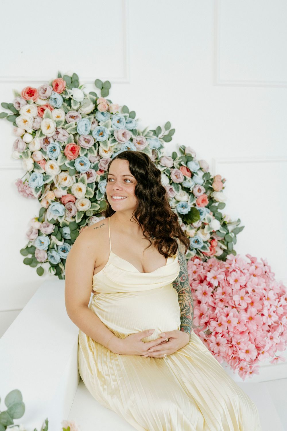 A maternity photo with a soft floral arch backdrop and delicate cream-colored dress.