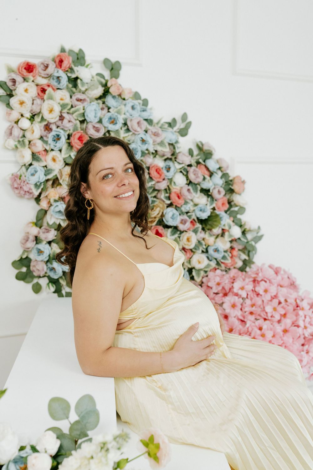 An elegant maternity portrait against a white wall with pink and blue floral decorations.