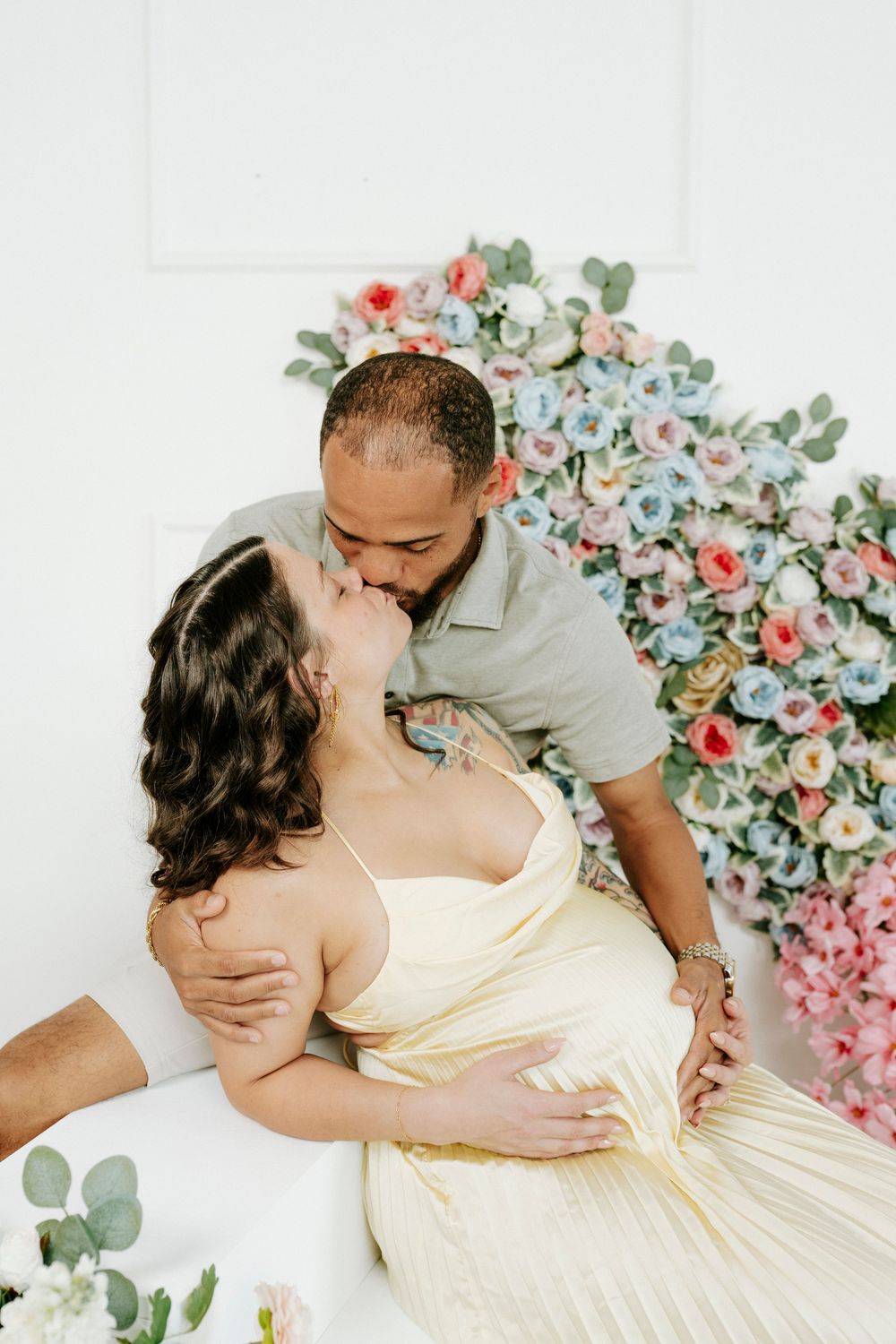 An intimate maternity photography session featuring a couple posing against a floral backdrop with pink roses.