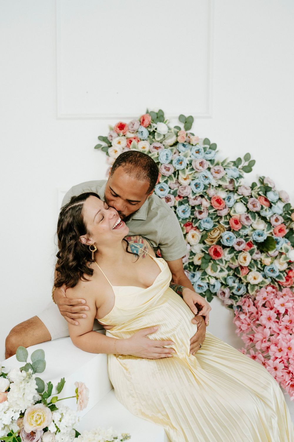 Couple poses romantically on white floor with colorful floral backdrop.