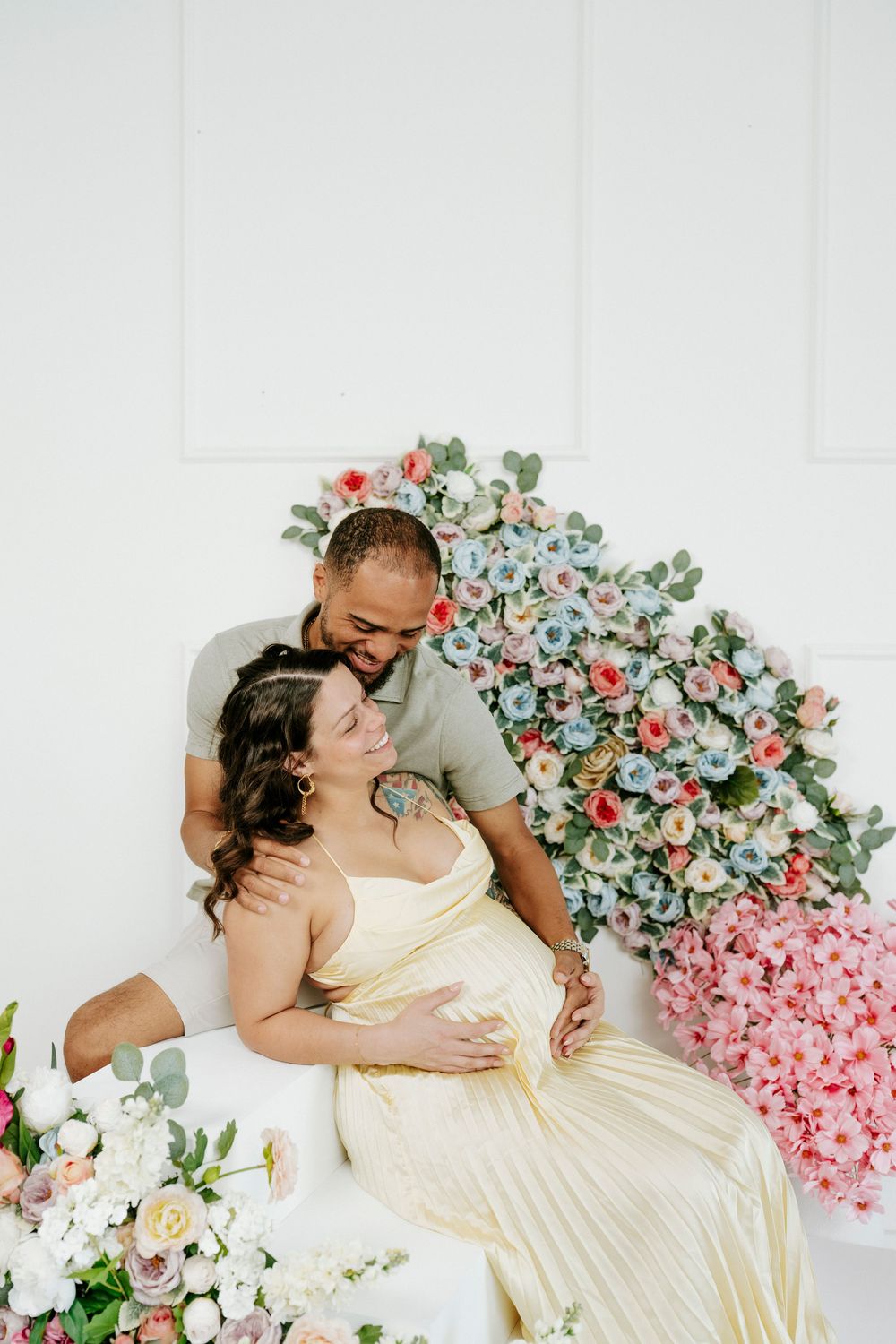 Couple embraces on floor with pink and blue floral wall decoration.