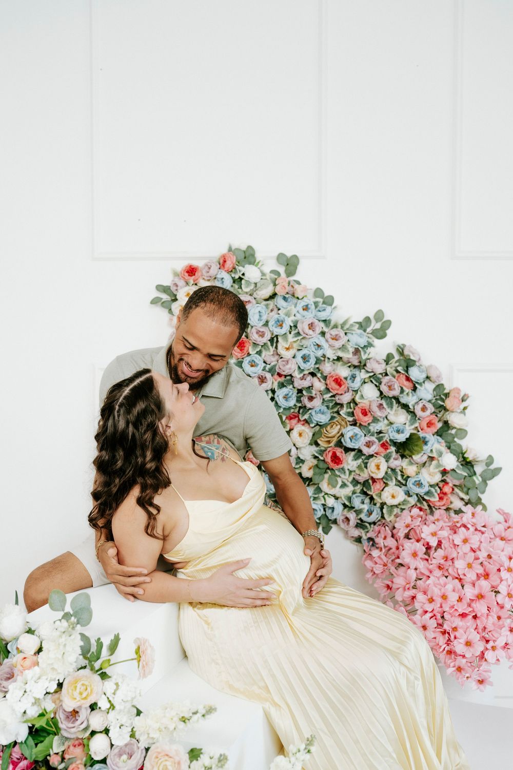 Loving couple shares tender moments against floral wall installation.