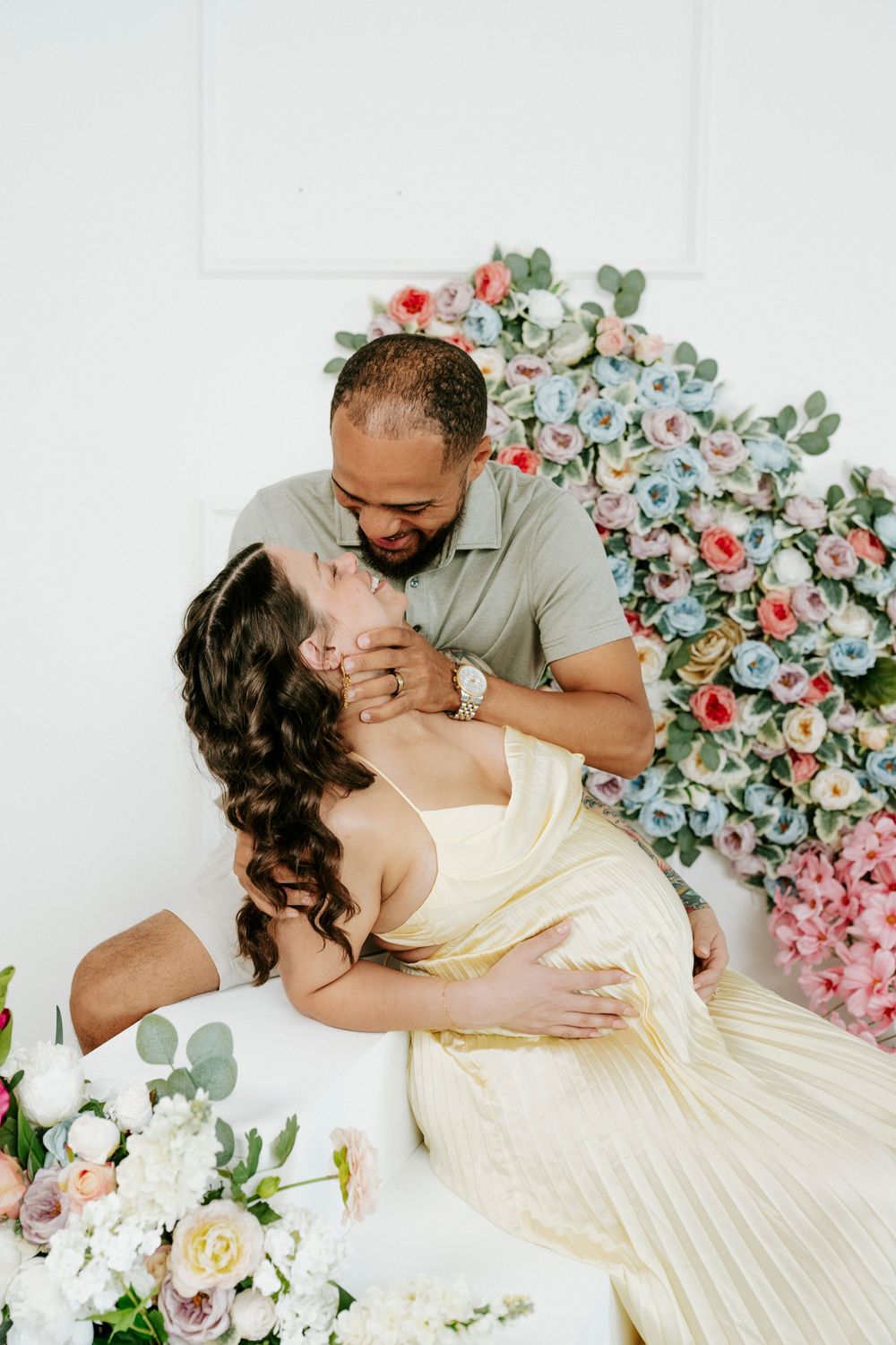 A romantic couple's portrait with floral decorations and a cream-colored dress against a white backdrop.