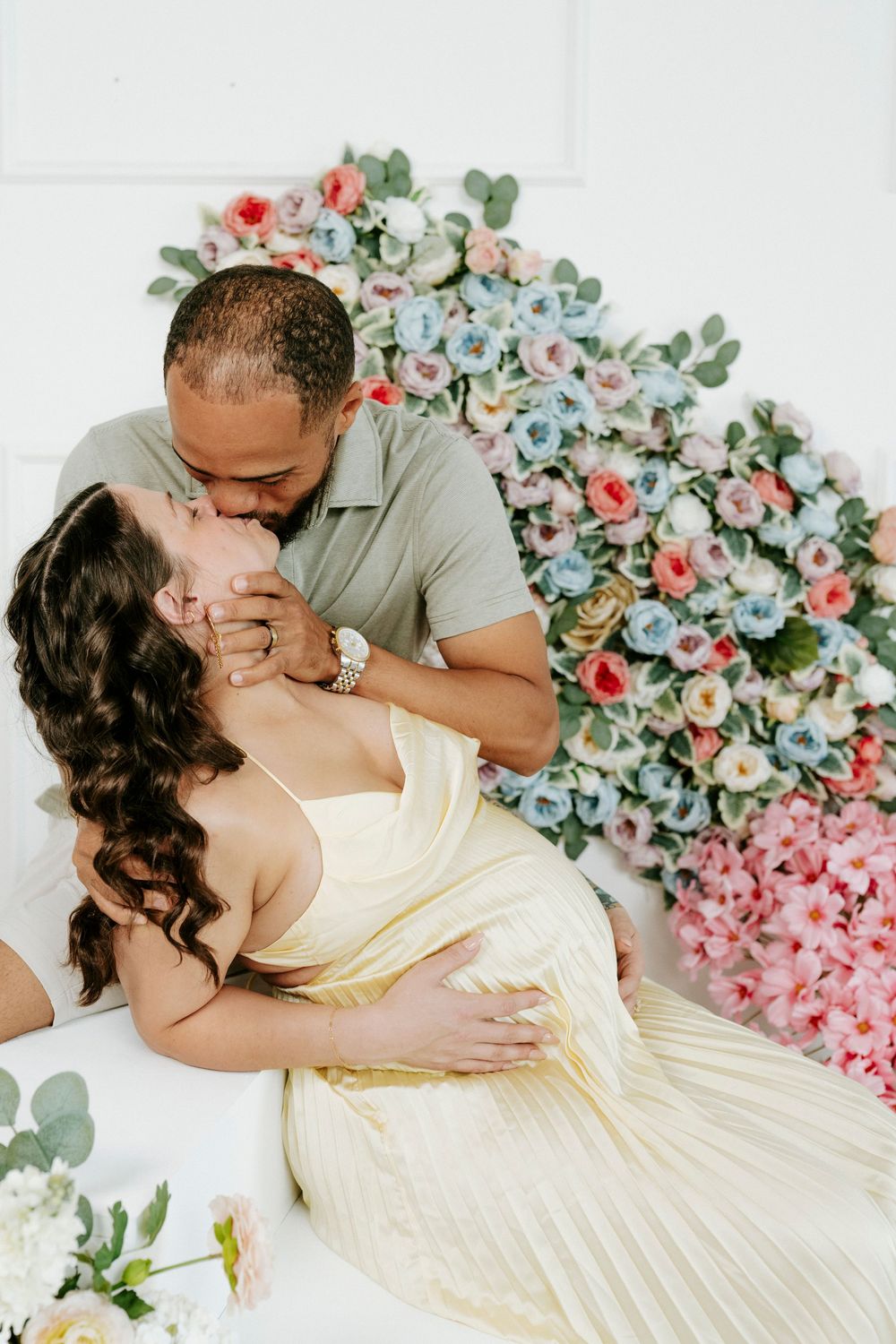 Romantic couple embraces against floral backdrop with pink and coral roses and eucalyptus leaves.