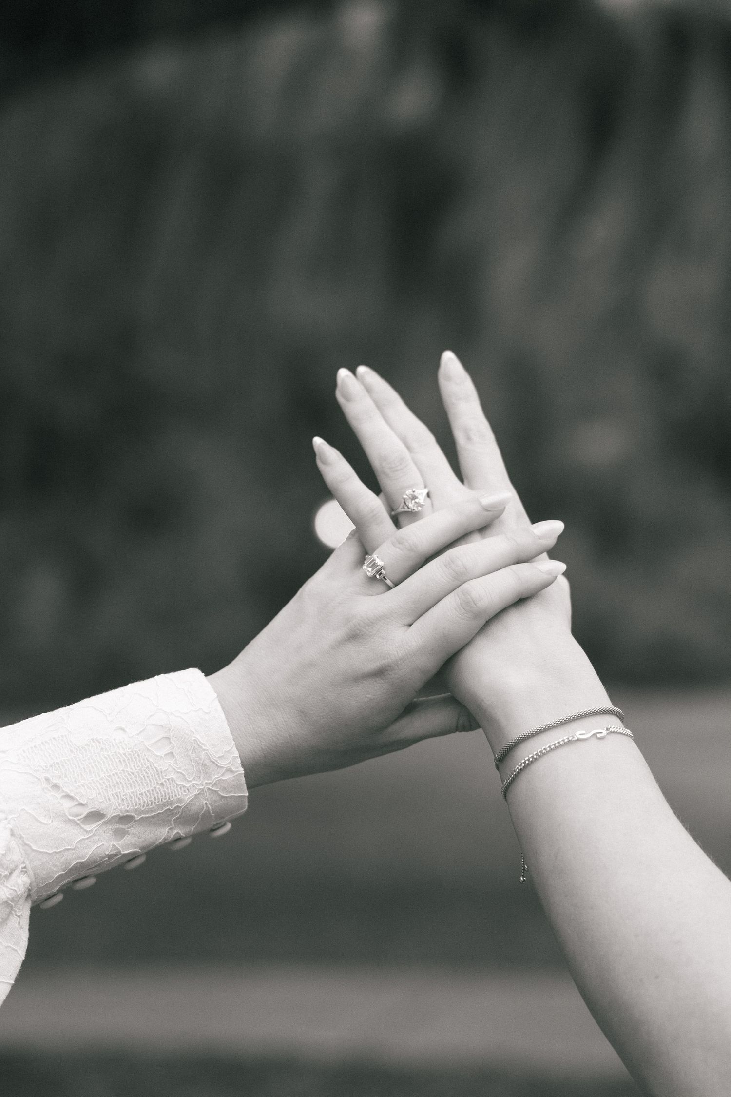 Black and white photo of two hands touching, adorned with rings and a bracelet, symbolizing love and connection.