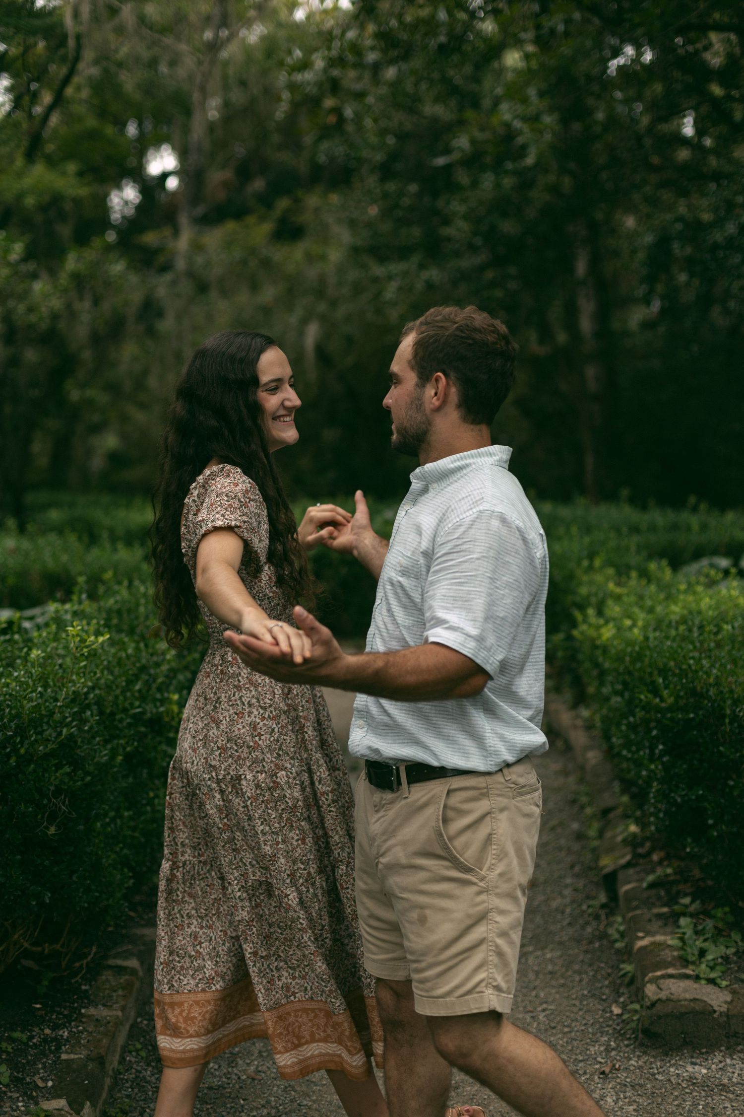 A couple shares a lighthearted dance moment on a garden path surrounded by greenery.