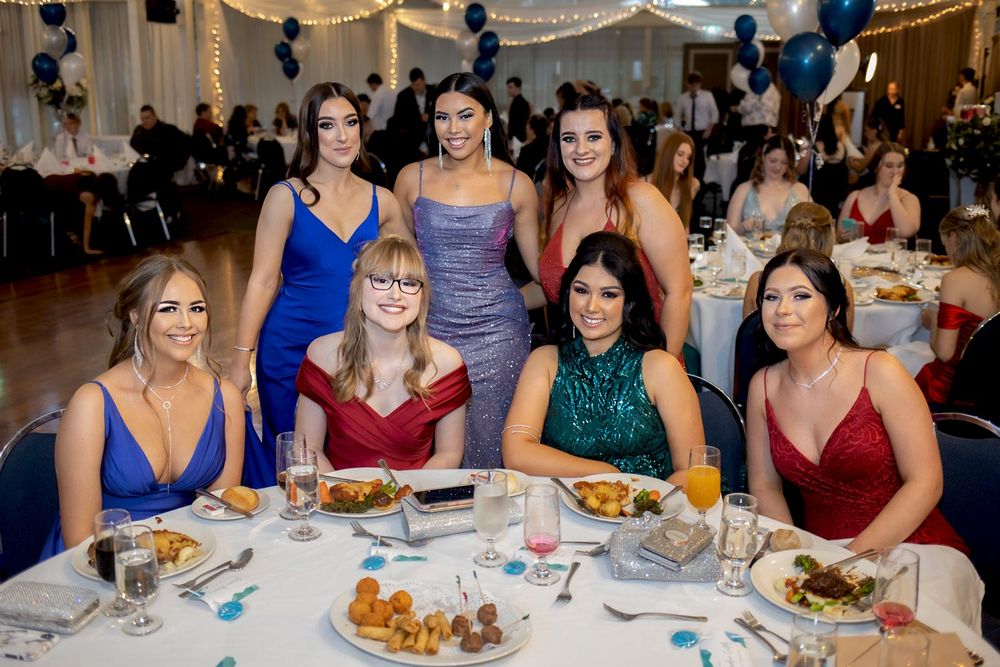 Sydney Event Photography - A group of friends in formal evening gowns gather around a dining table at an elegant event.