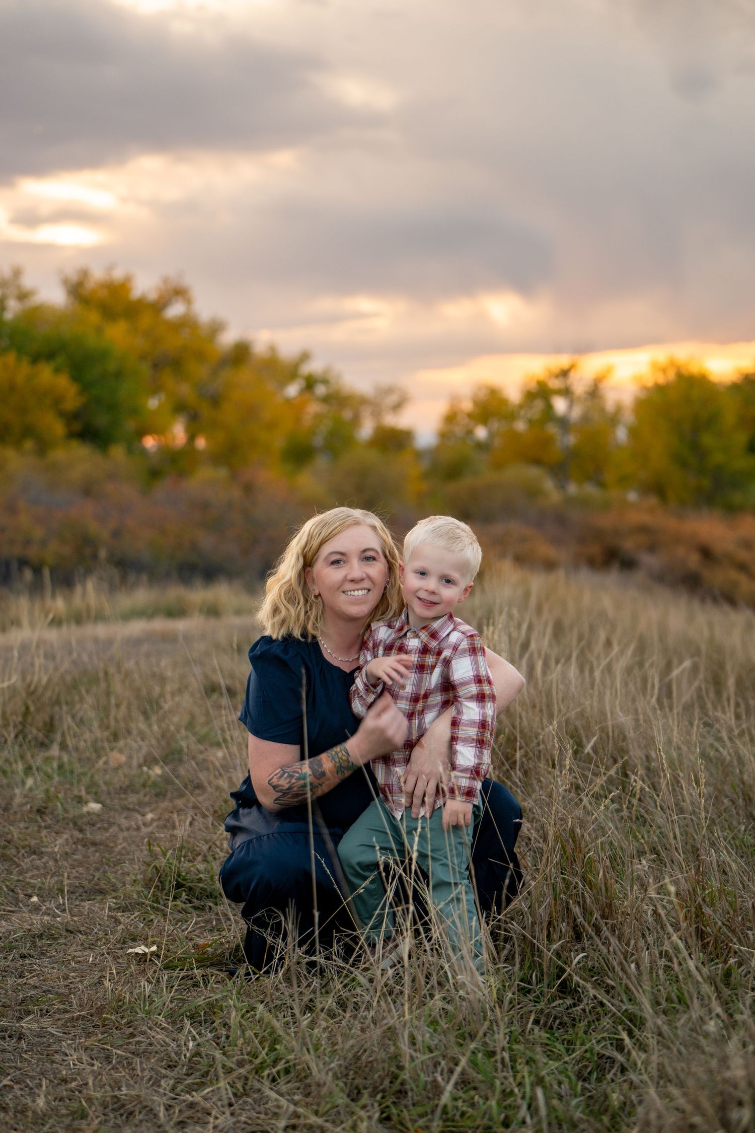 A tender moment captured at sunset in a golden field with autumn trees in the background.