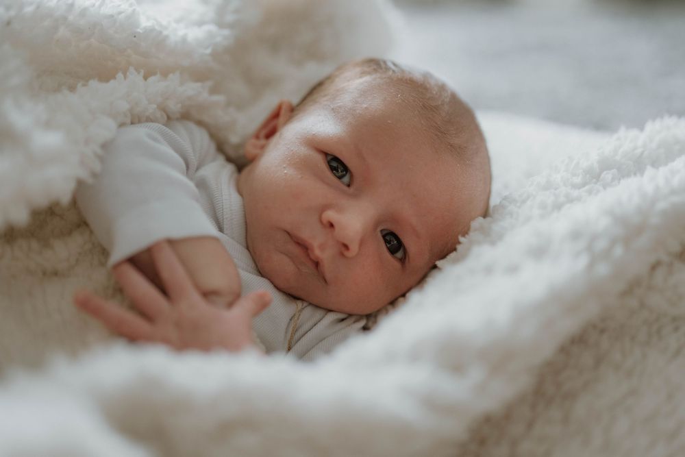A small baby rests peacefully on soft white bedding while wearing light colored clothing.