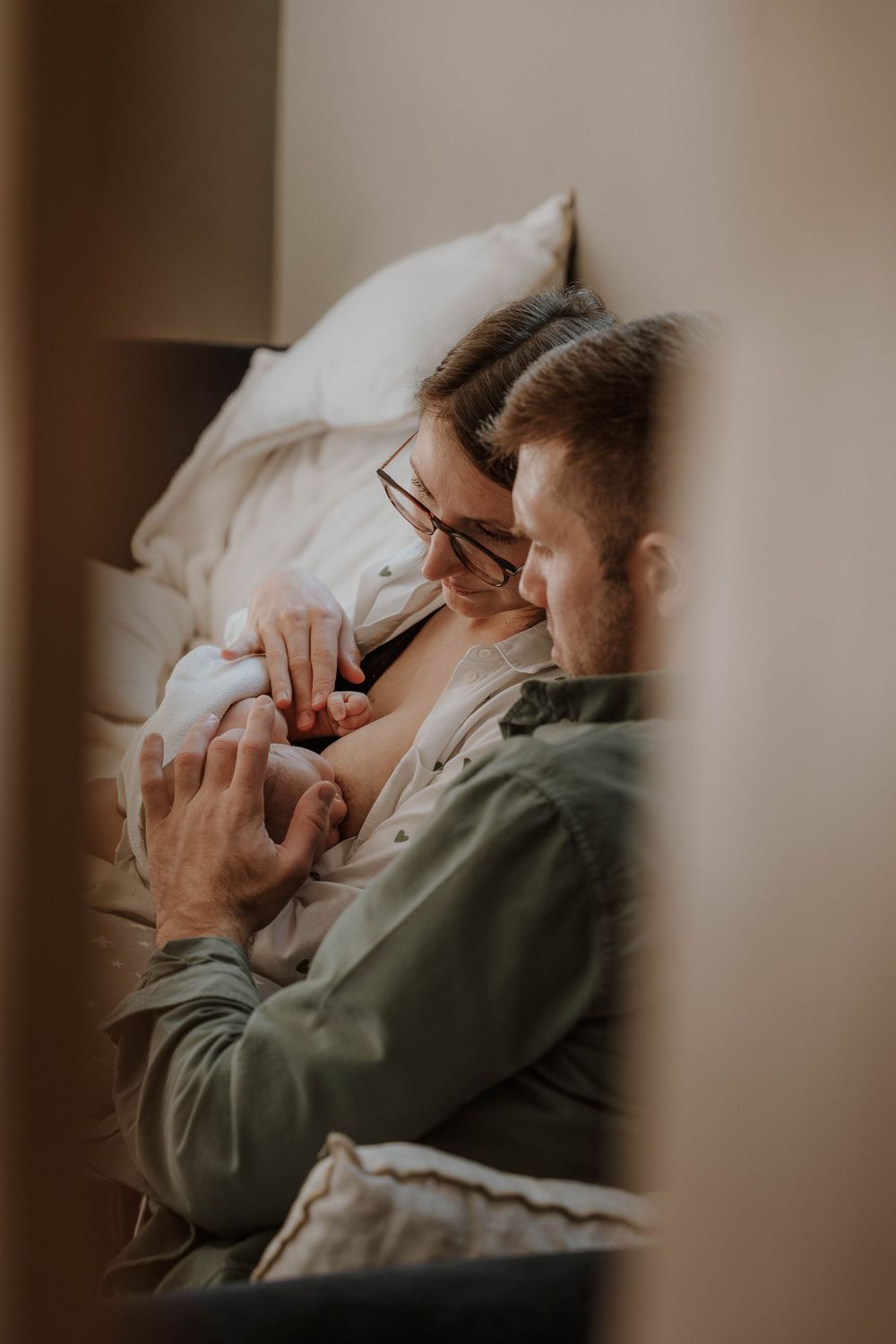 New parents tenderly holding their newborn baby together while resting in bed at home.