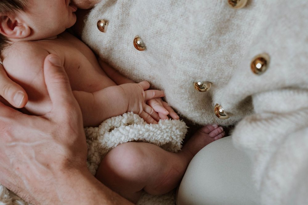 A tiny hand gently touches a soft white teddy bear against a neutral background.