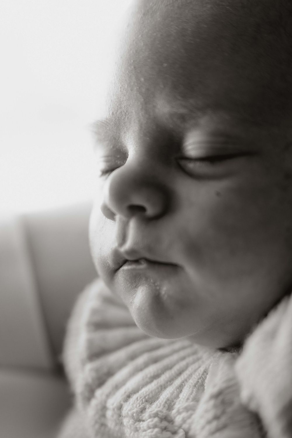 Black and white close-up portrait of a sleeping newborn baby with chubby cheeks wearing a knit sweater.