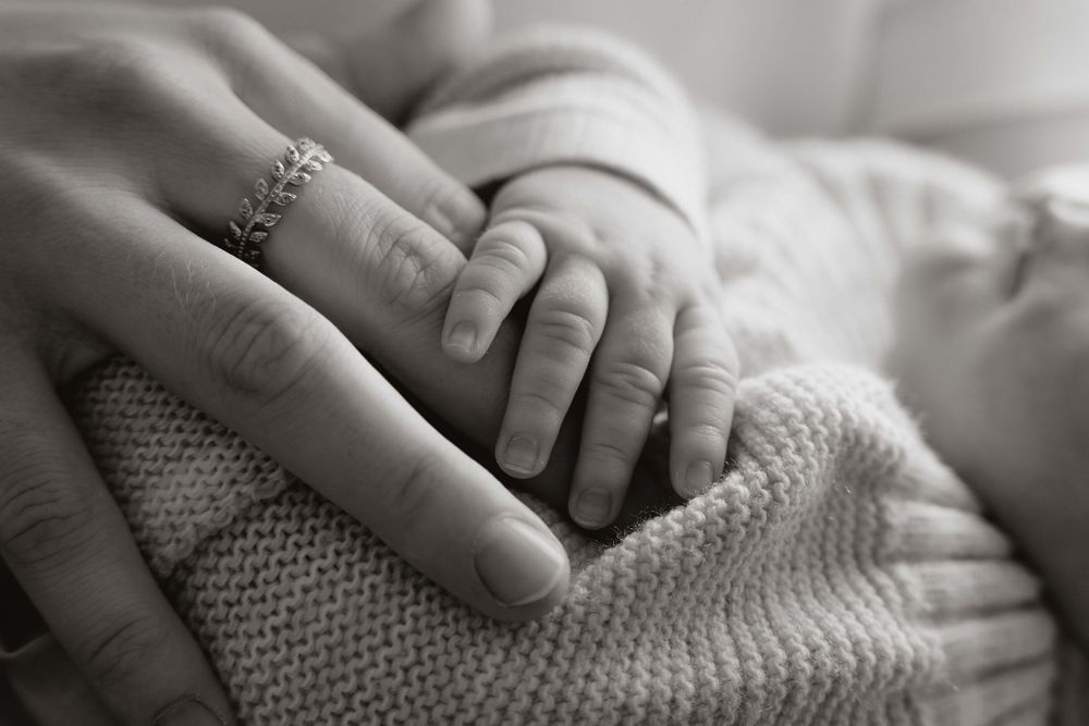 Black and white photo of a newborn baby's hand resting on a mother's hand wearing a diamond ring.