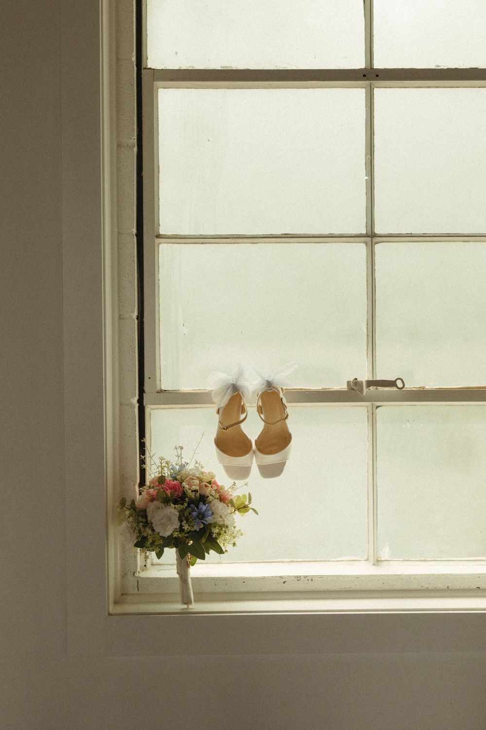 Wedding shoes and floral arrangements sit on a sunlit windowsill creating a romantic atmosphere.