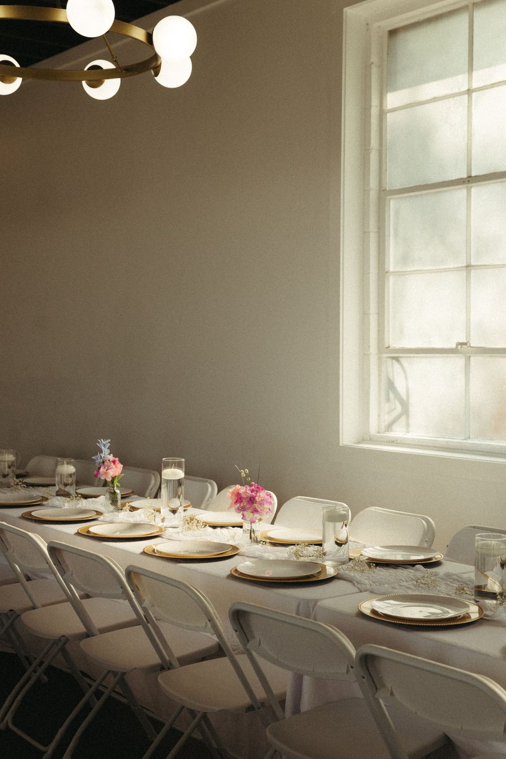 A minimalist wedding reception table setting with white folding chairs and place settings.