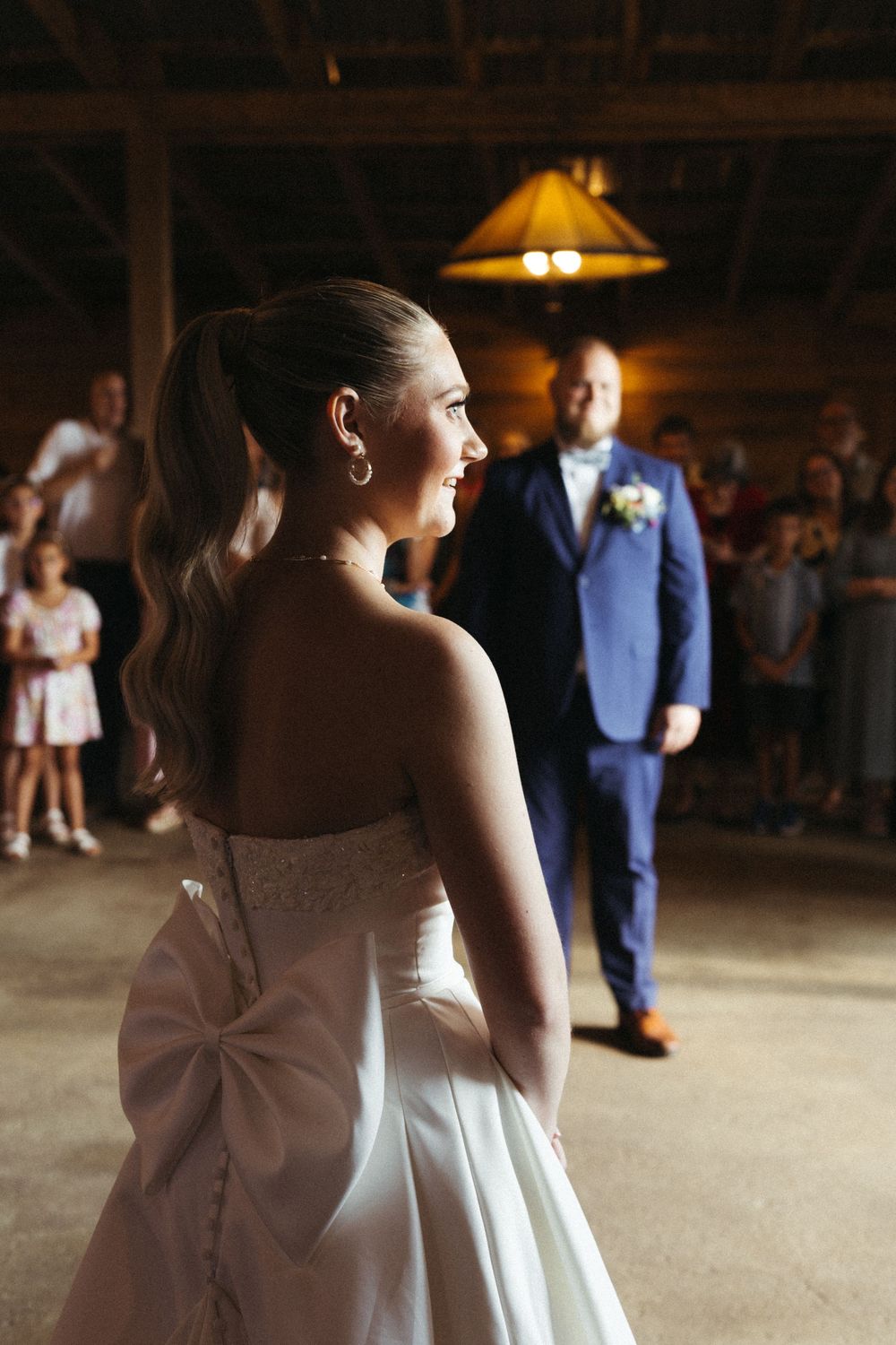 A bride in a white gown with a bow detail dances in an indoor venue during a wedding reception.