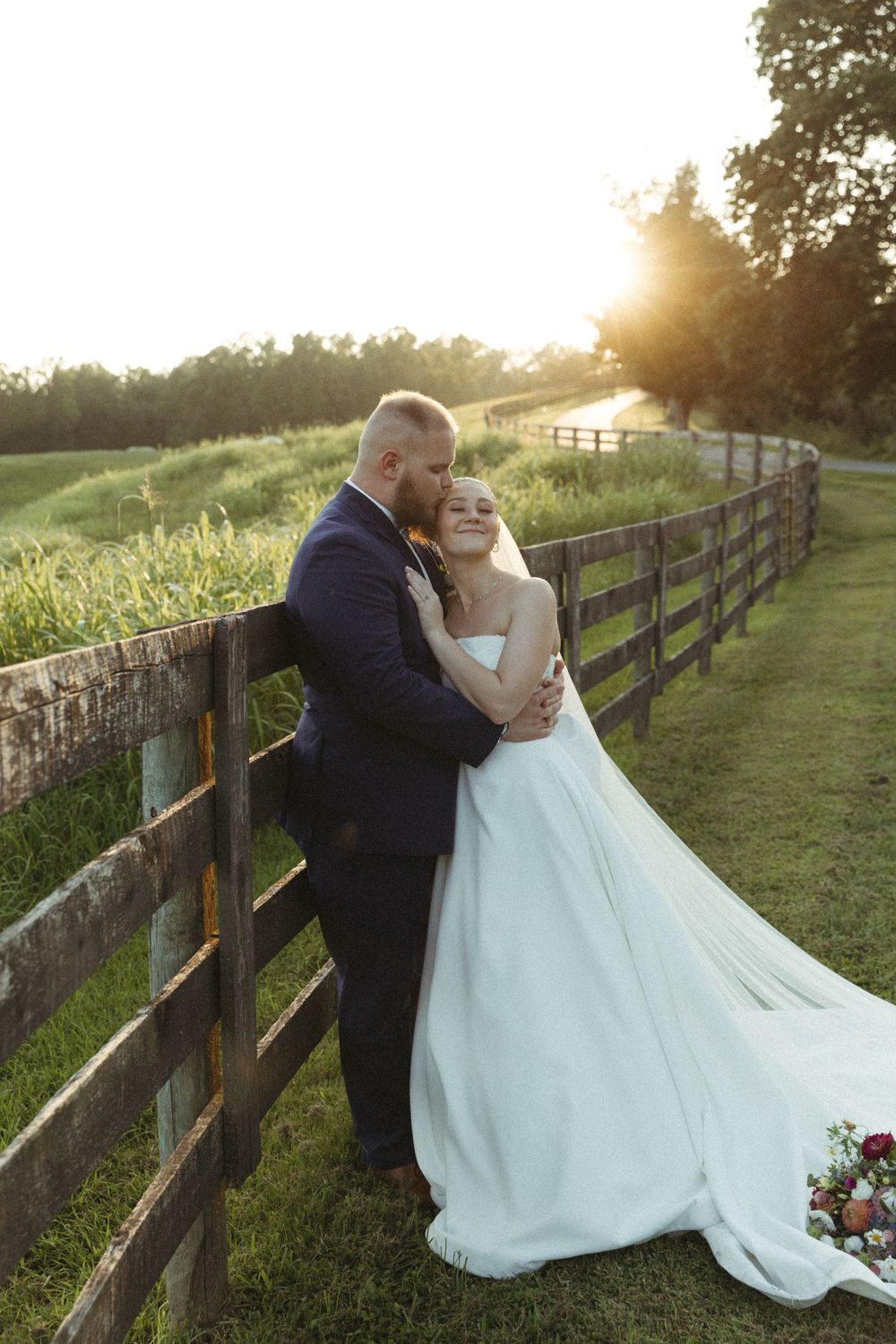 A couple shares an intimate moment against a rustic wooden fence during golden hour.