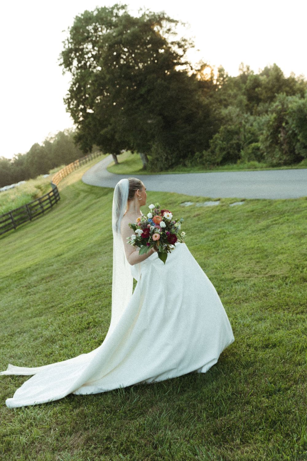 Wedding dress flowing dramatically on green hillside during sunset photoshoot.