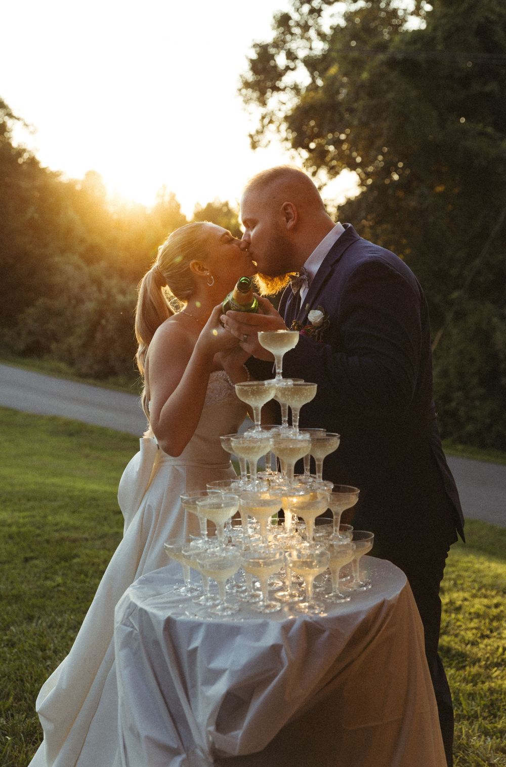 A couple poses with a champagne tower at sunset during their wedding celebration.