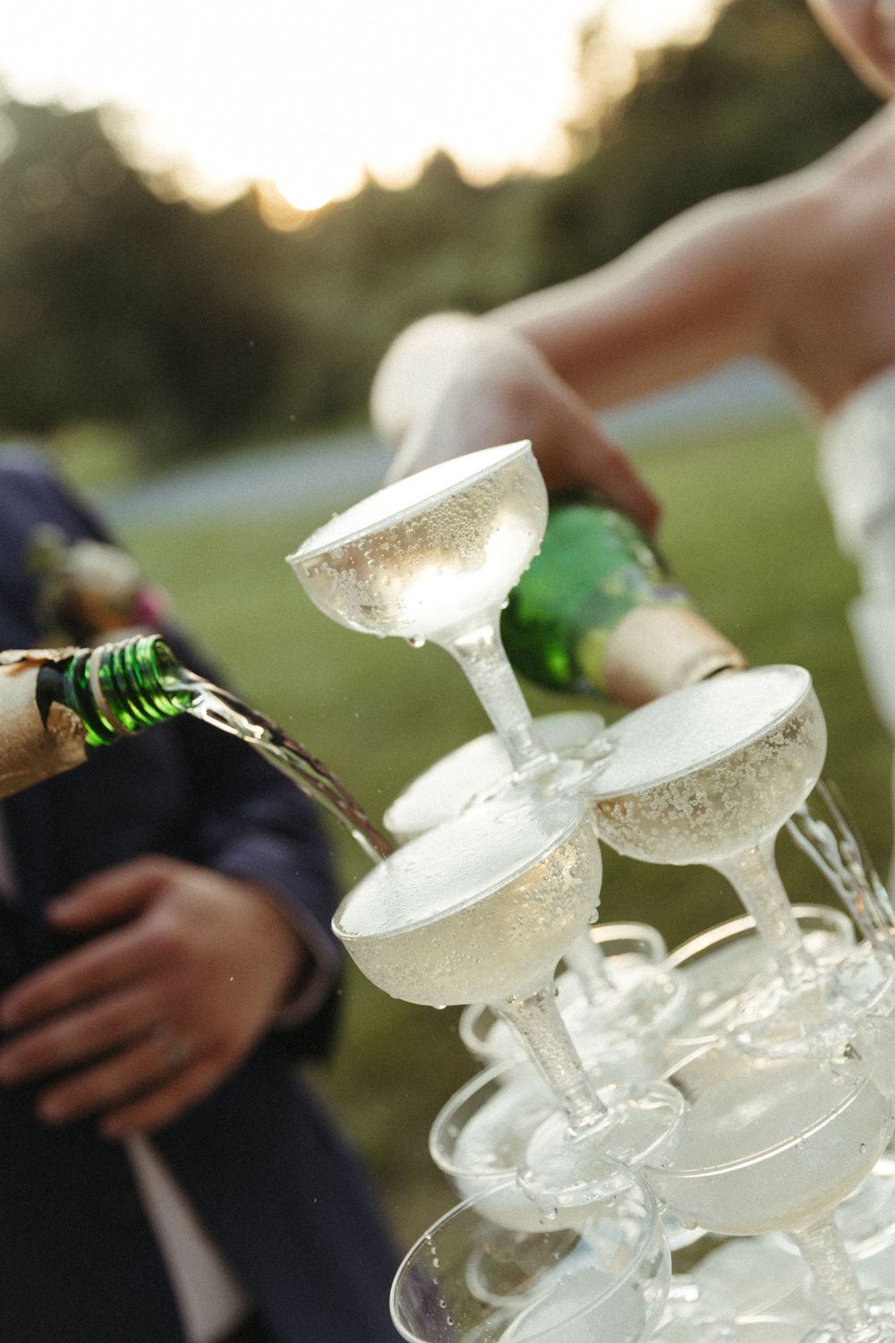 Champagne being poured into an elegant tower of crystal glasses at an outdoor wedding reception.