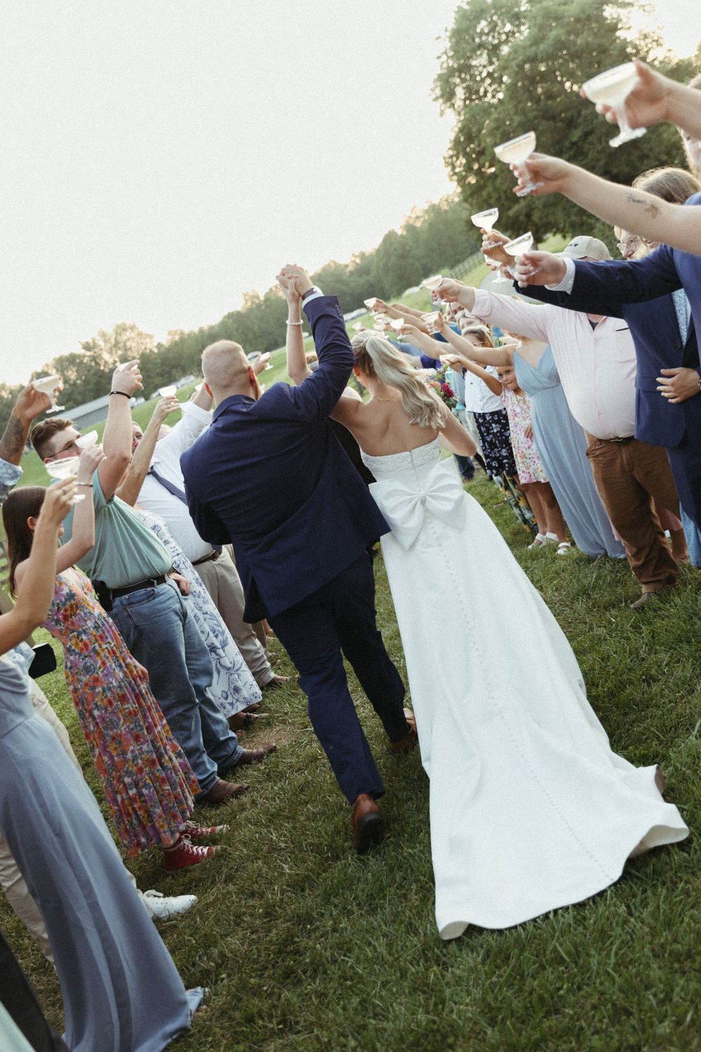 Wedding guests raise their glasses in a celebratory toast outdoors at dusk.