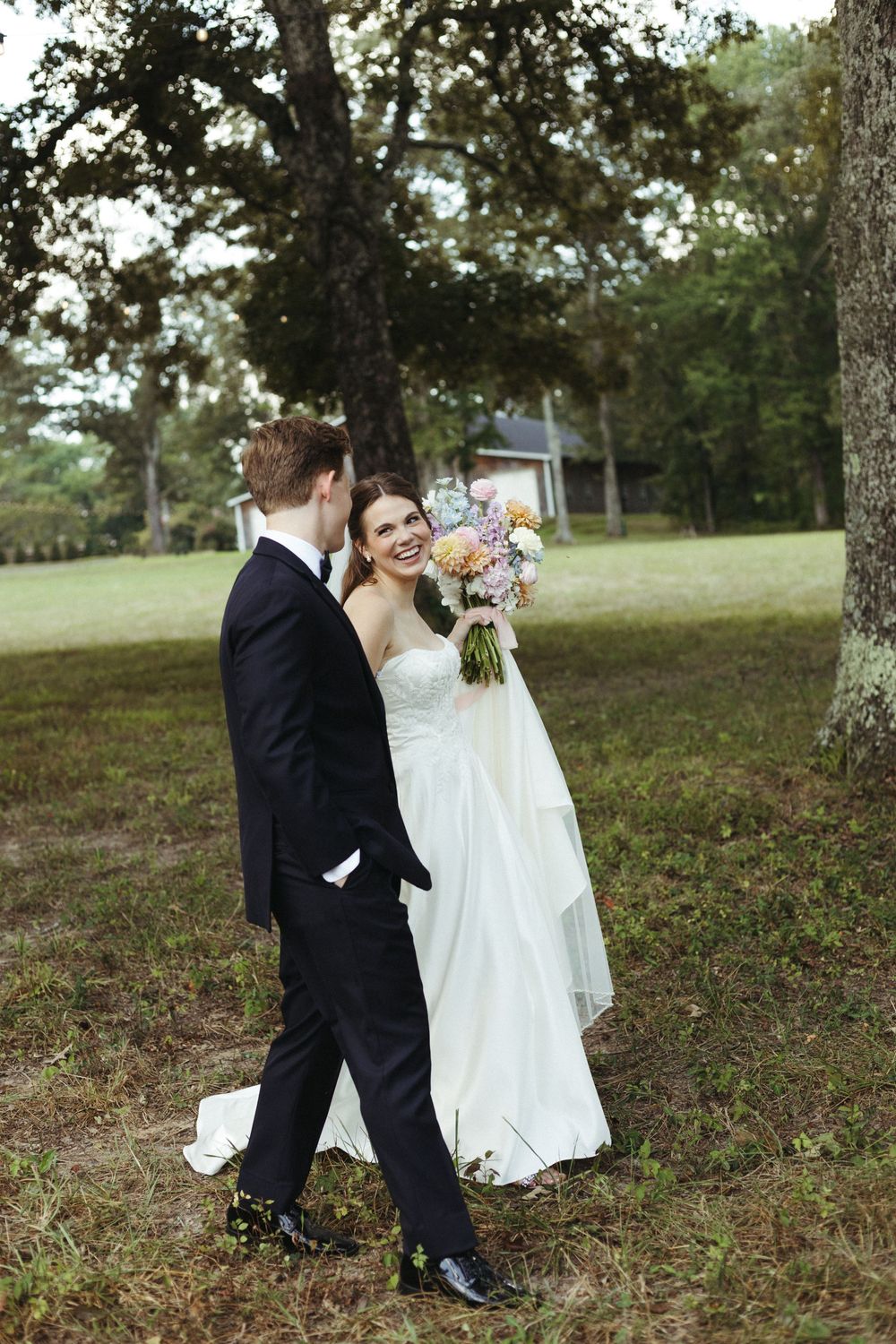 Wedding couple shares intimate moment on grassy hillside under trees.