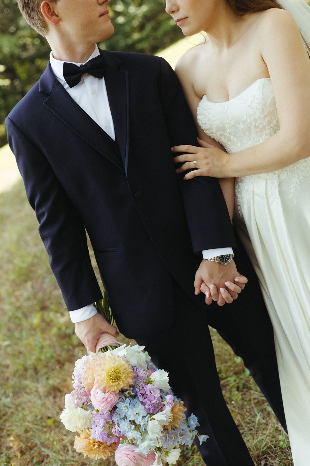 Couple in formal wedding attire holding colorful pastel bouquet in outdoor setting.