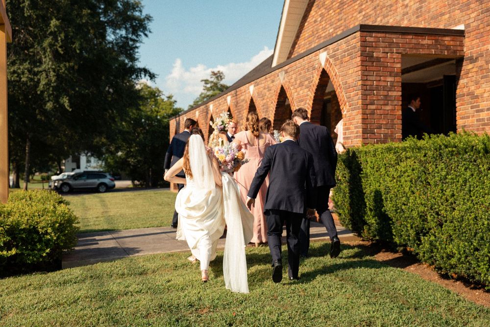 Wedding party gathered outside brick church on sunny afternoon.